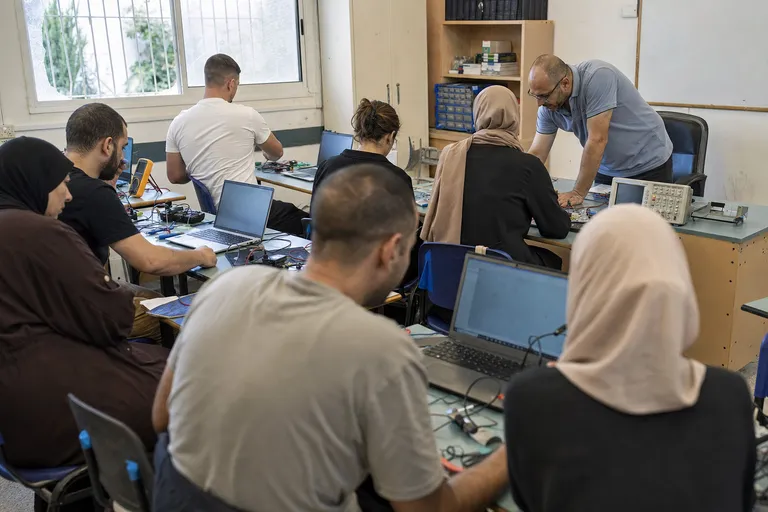 לומדים בכיתת הכשרה מקצועית עובדים על מחשבים וציוד אלקטרוני.