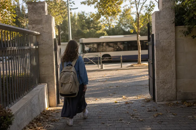 תלמיד עם תיק גב בדרך לבית הספר, כשאוטובוס חולף ברקע.