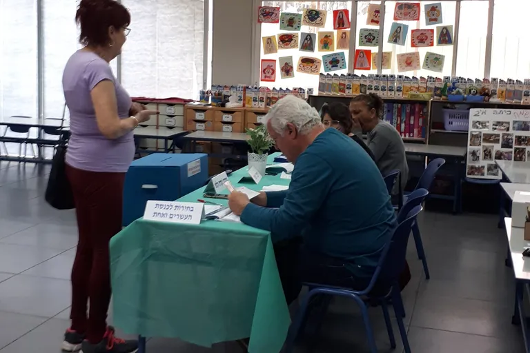 מצביעה בקלפי בבחירות בישראל לצד חברי ועדת הקלפי