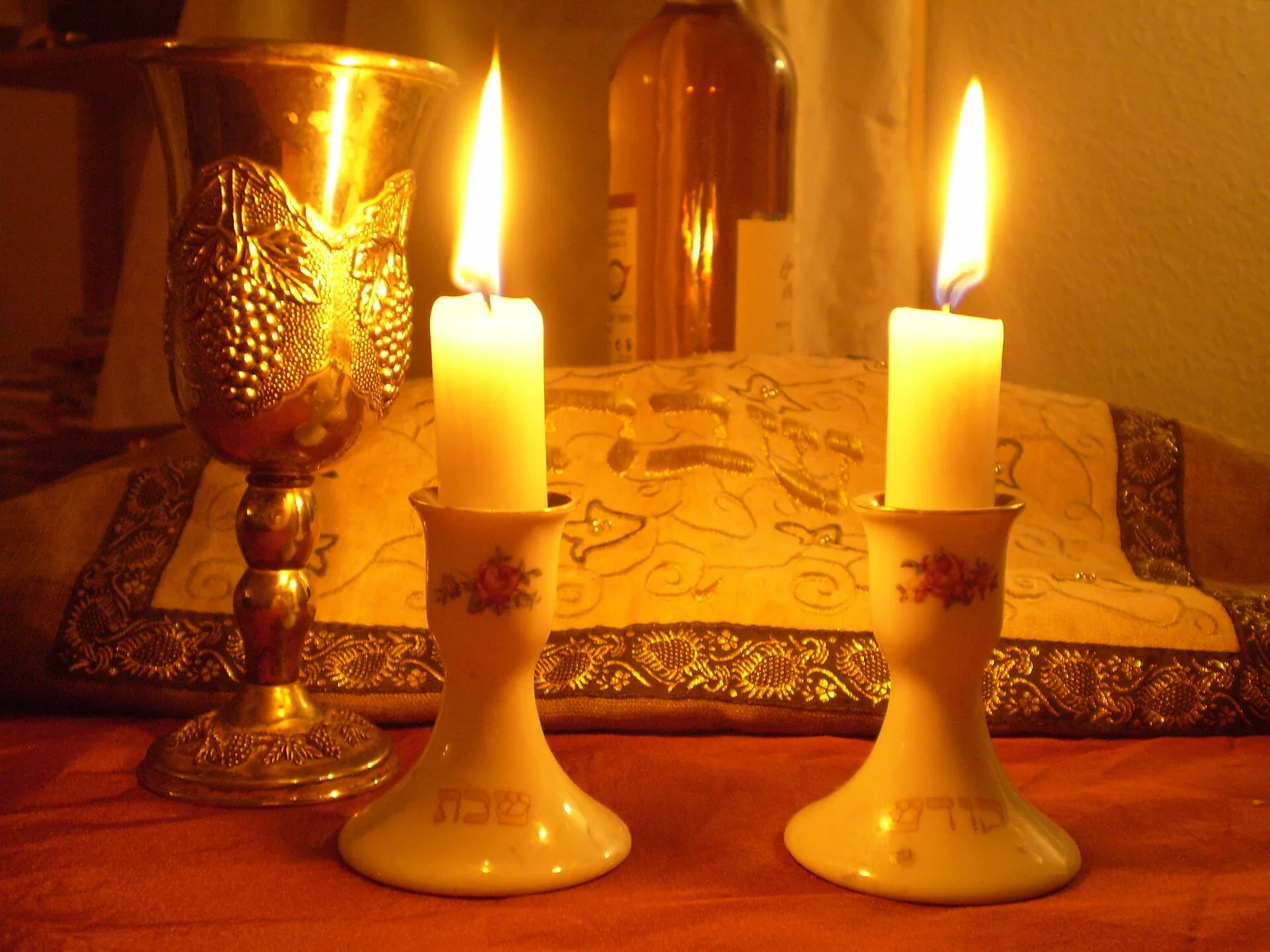 נרות שבת דולקים לצד גביע קידוש וחלה