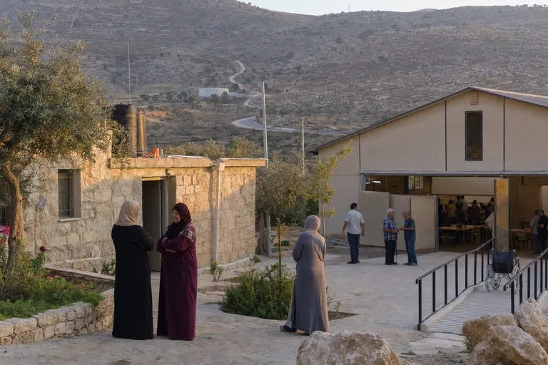 חצר כפרית בשומרון ובה מבנה קהילתי סמוך לעצי זית.