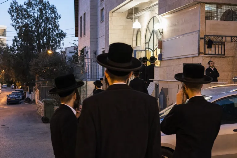 גברים חרדים עומדים בשקט סמוך לבית כנסת במודיעין עילית.